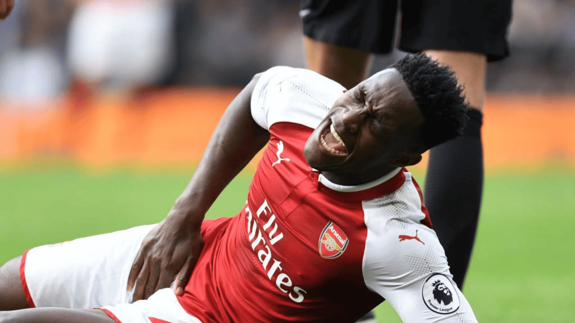 soccer player in red and white arsenal kit lying on grass holding groin in pain grimacing during match