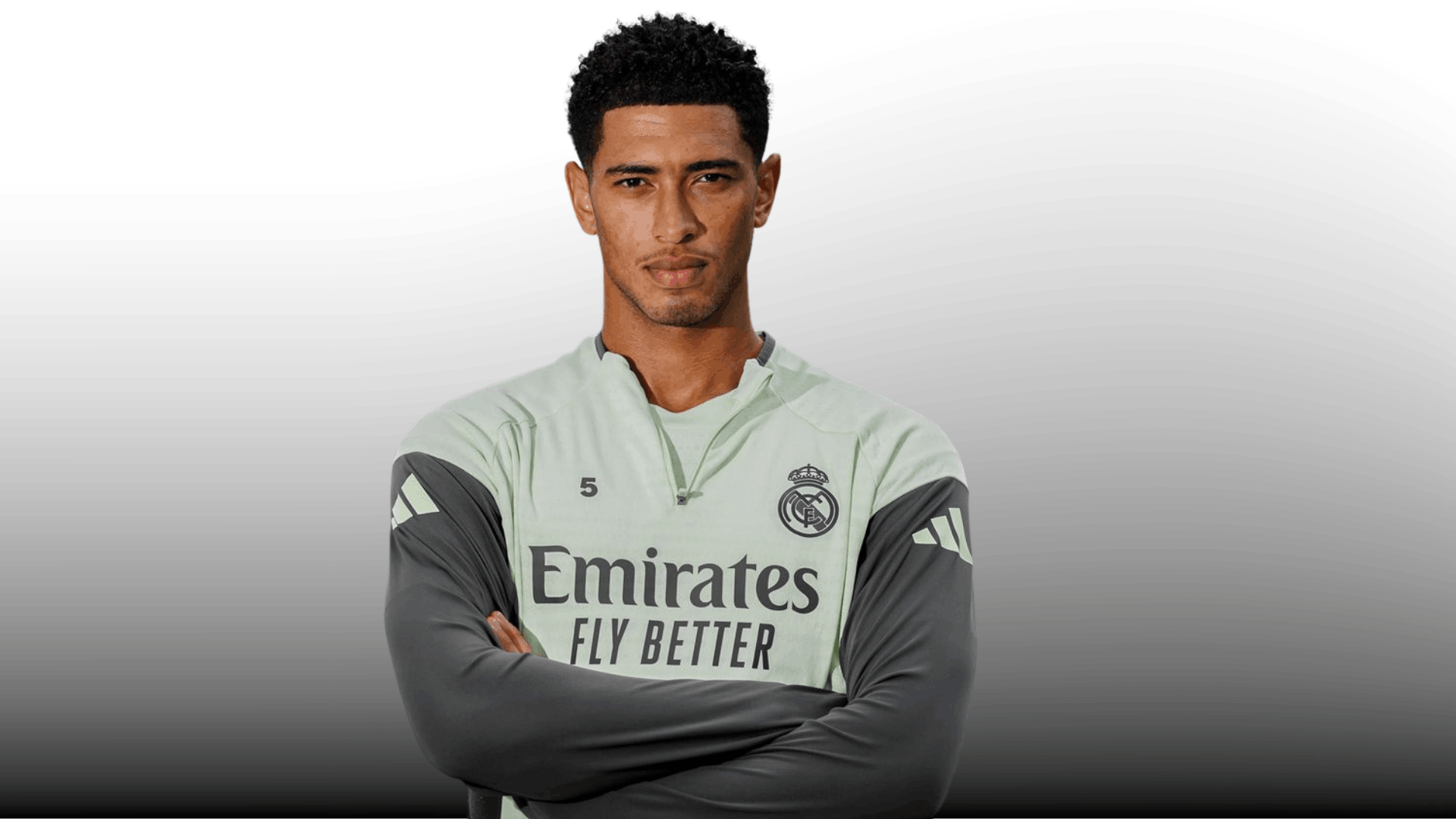 soccer player in training kit showing a short curly taper fade with arms crossed on a plain background
