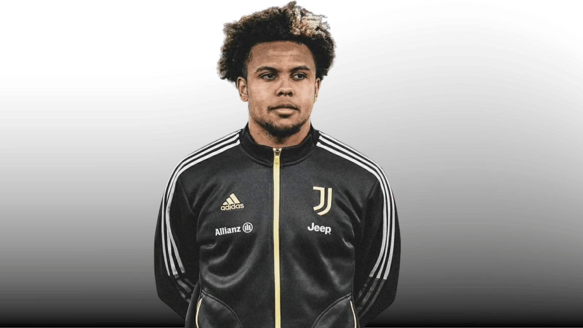 soccer player with full afro haircut and blond highlight wearing black training jacket on gray background