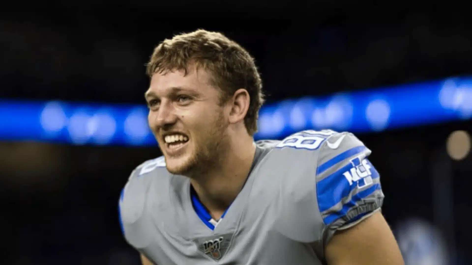 tj hockenson smiling on the sideline wearing a detroit lions jersey during a game