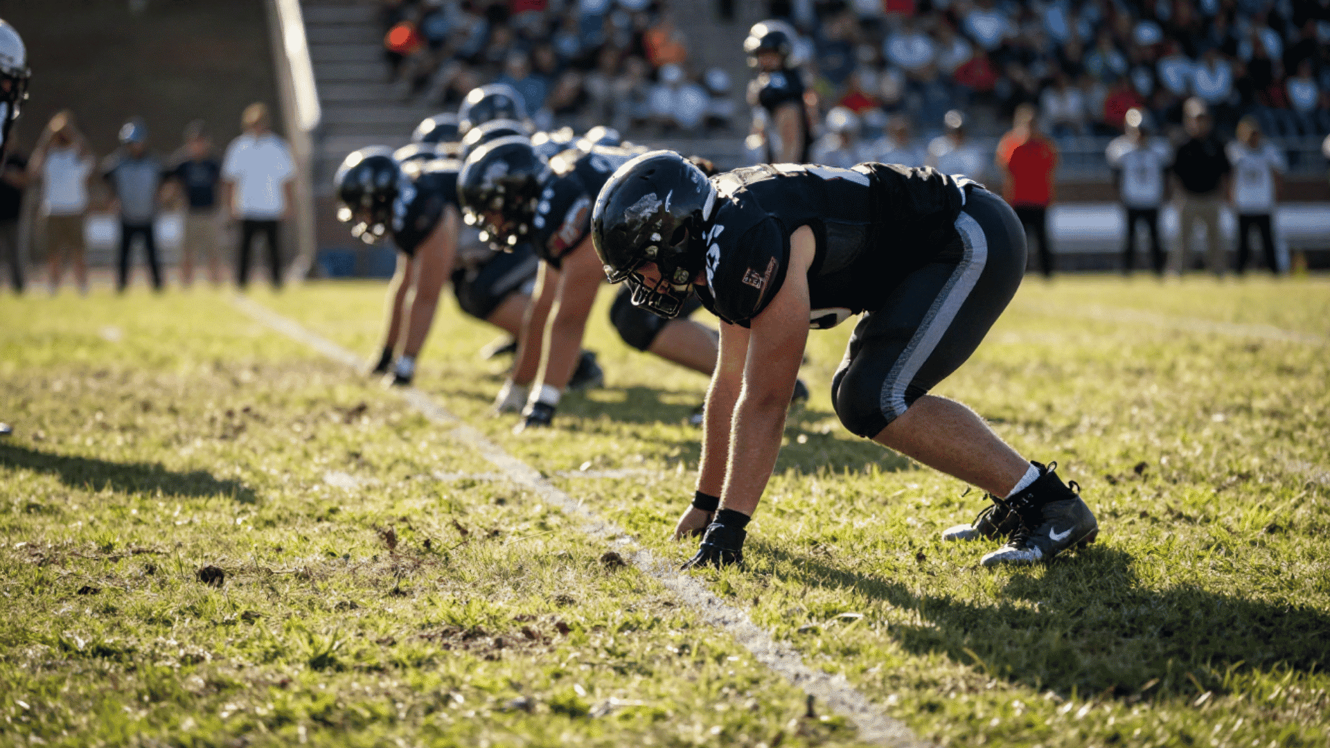 three football players in black uniforms in a defensive stance on the field