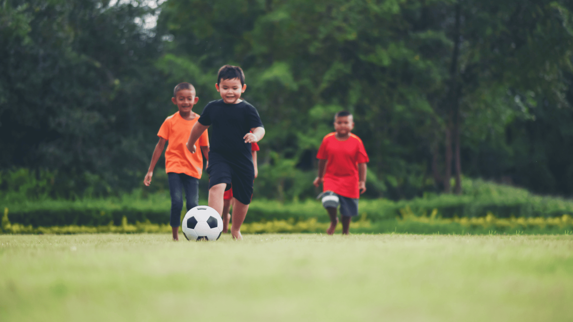 three young children running together on a bright green field playing happily with a classic black and white soccer ball