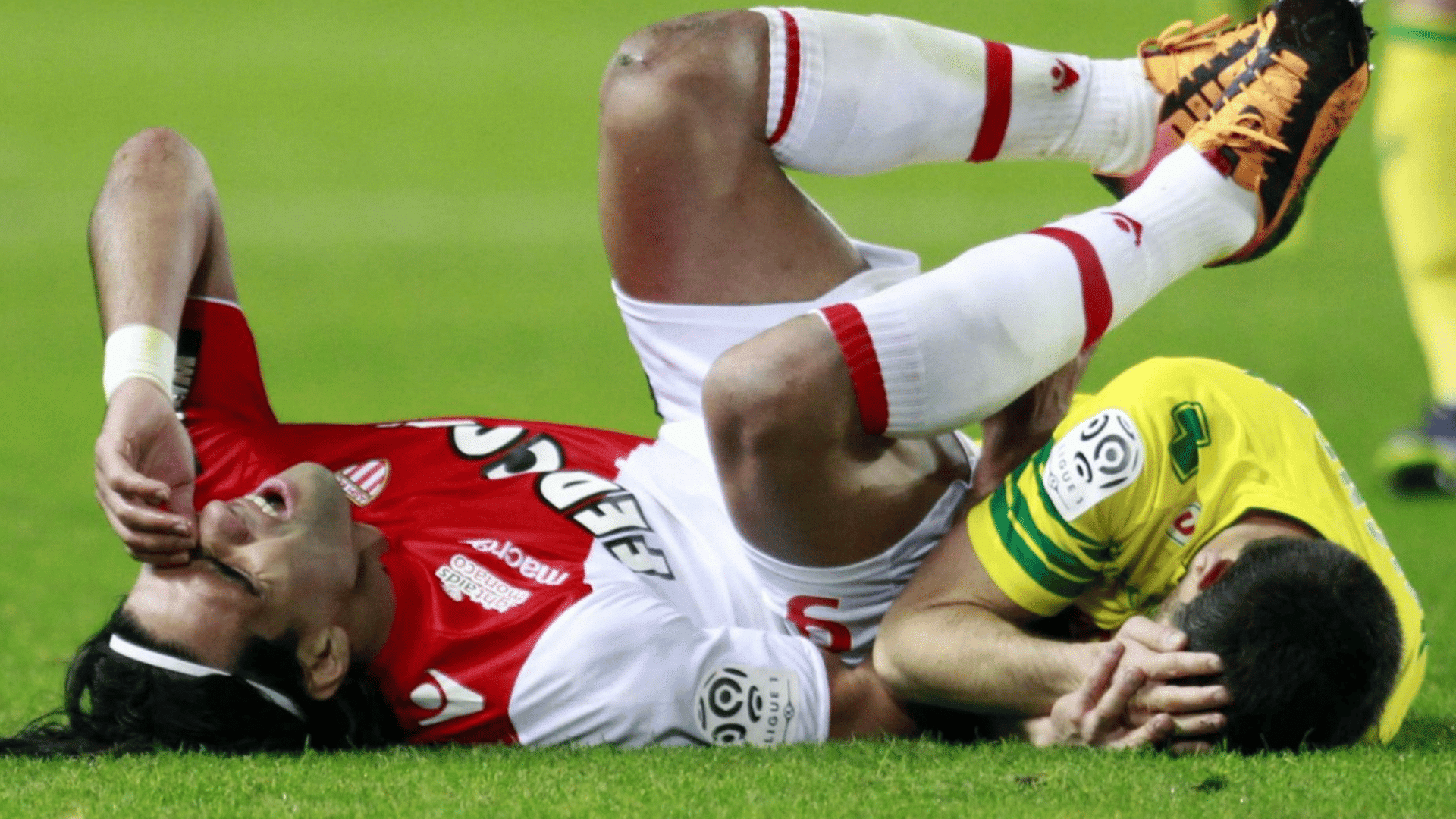 two football players lie on the grass clutching their faces after colliding during a match on the pitch