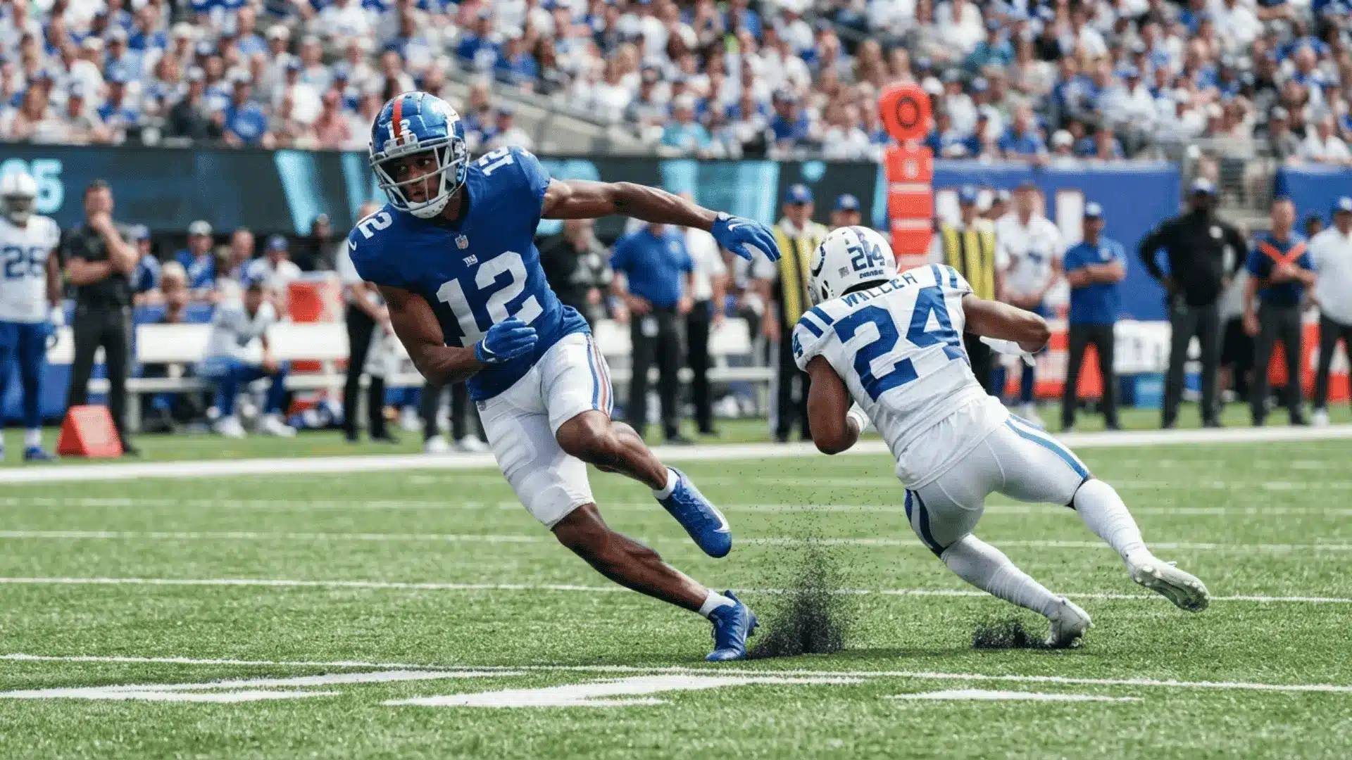 a football player in a blue uniform cuts across the field as a defender in white slips behind him near the sideline