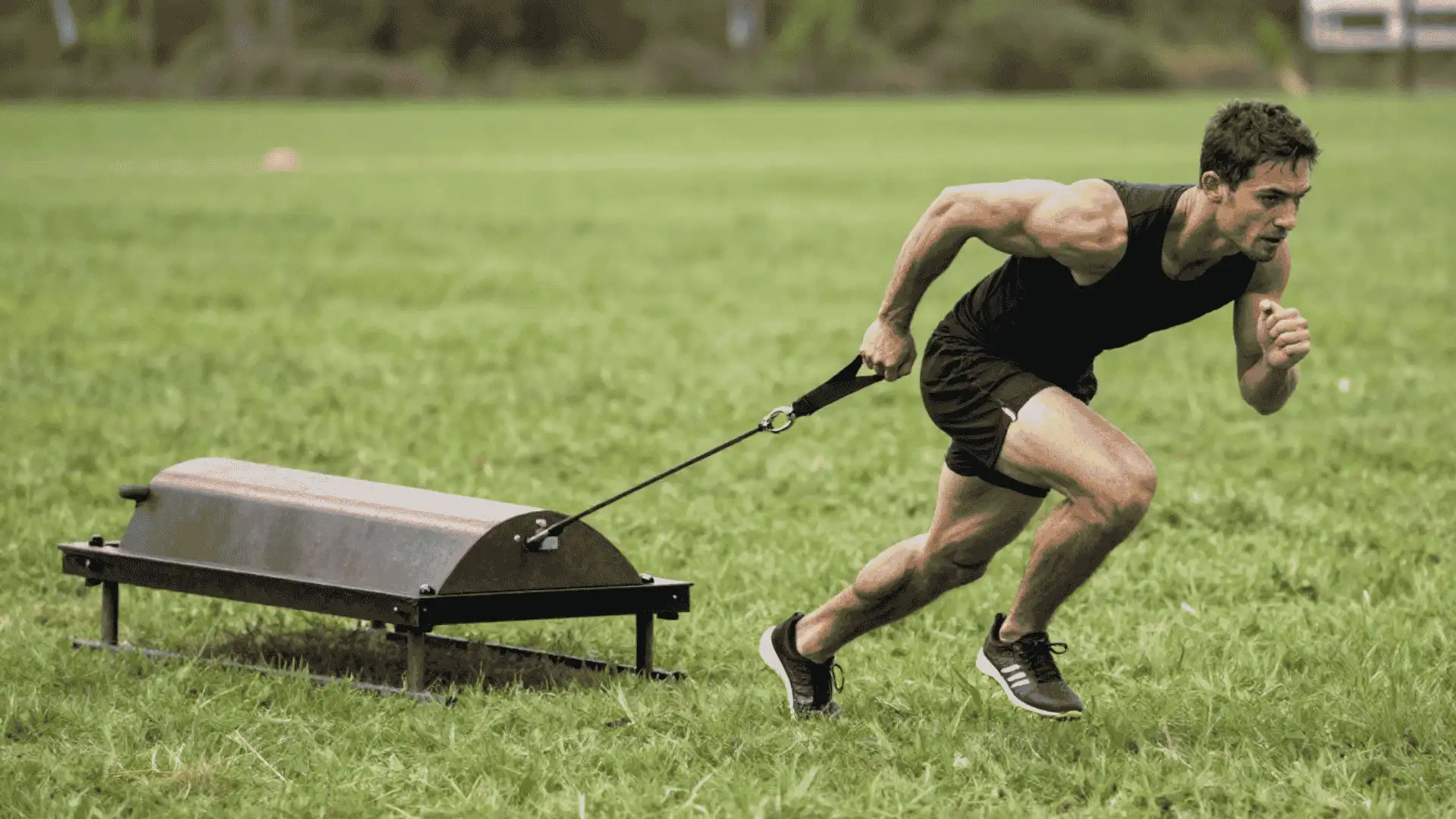 athlete sprinting forward while pulling a weighted sled across grass for power and acceleration training