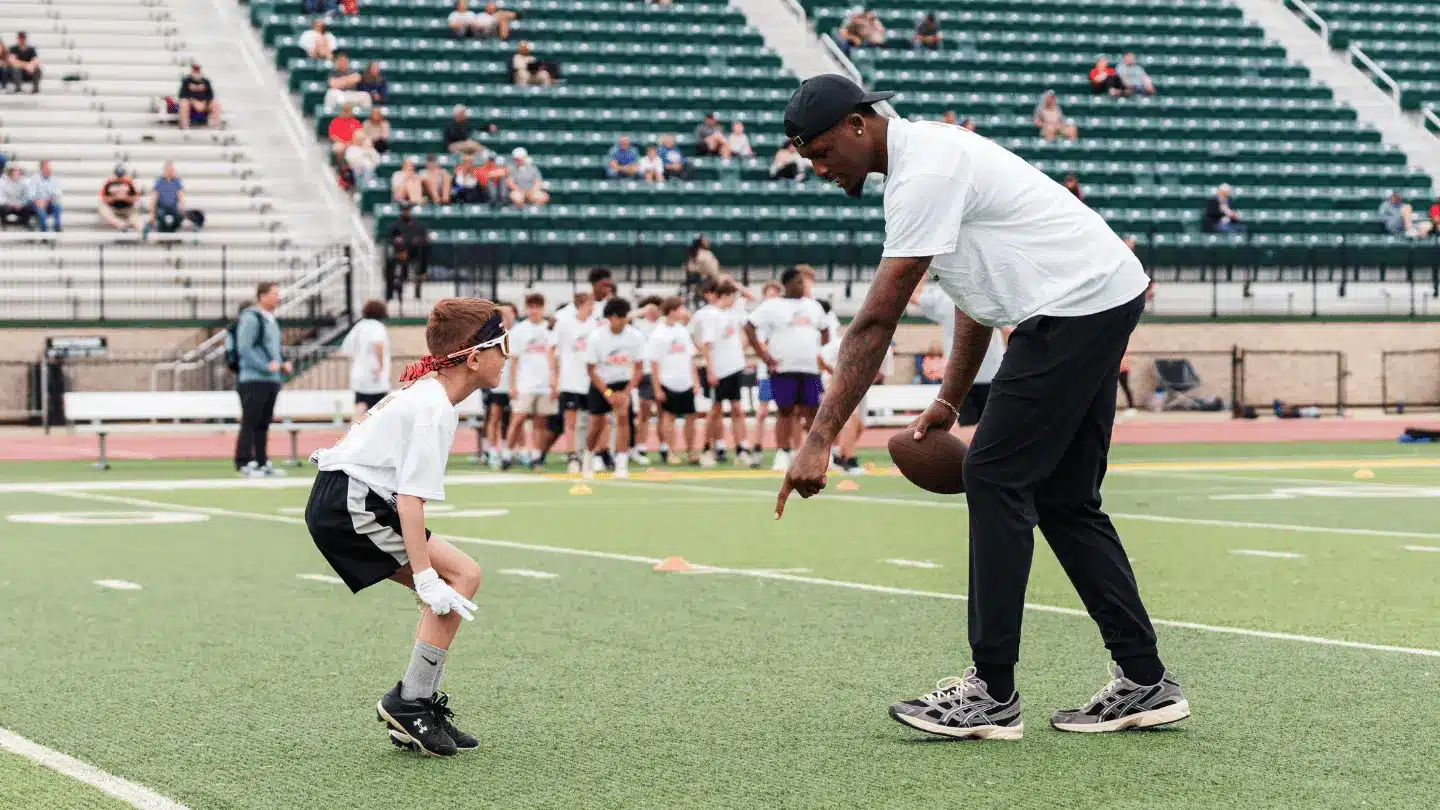 man holding football teaching kid to do drills in a bright green field with white jersey