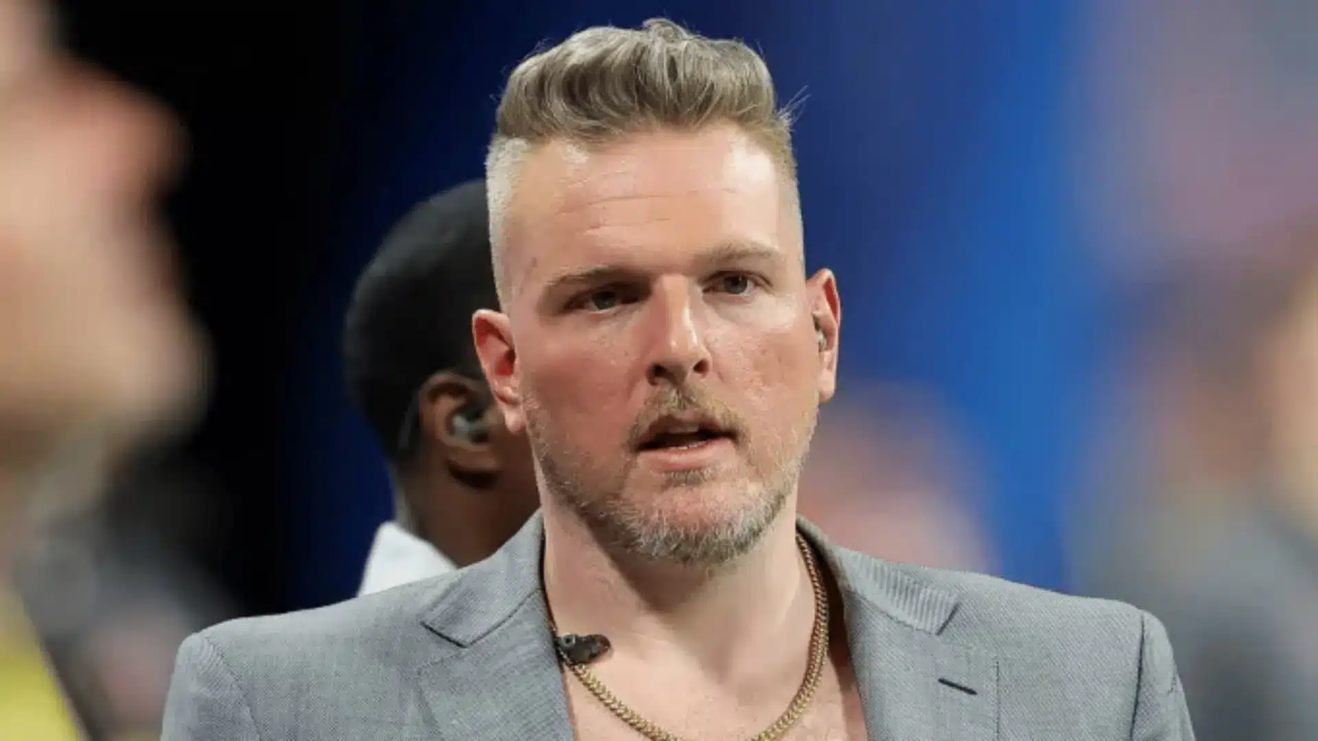 a close view of a man in a gray blazer wearing an earpiece and small microphone while standing at a crowded sports venue