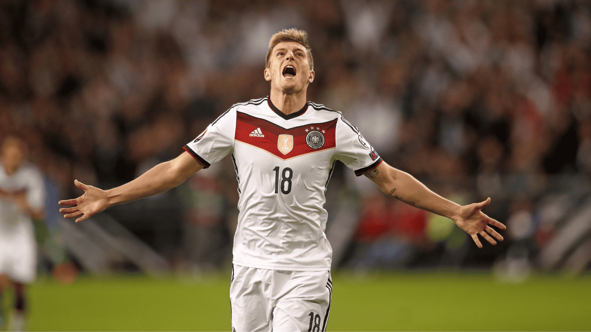 wide angle focus shot on toni kroos wearing his white jersey and celebrating a goal with his arms to the side