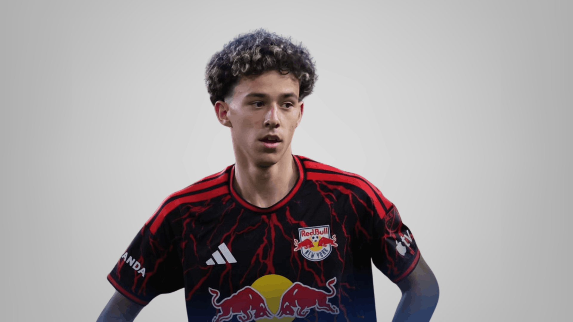 young ny red bulls soccer player wearing black and red jersey standing with hands on hips against plain gray background