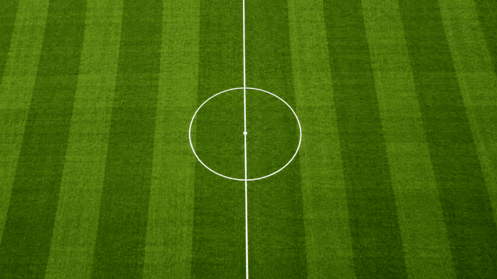 an aerial view shows the crisp white halfway line crossing the striped green soccer field through the center circle