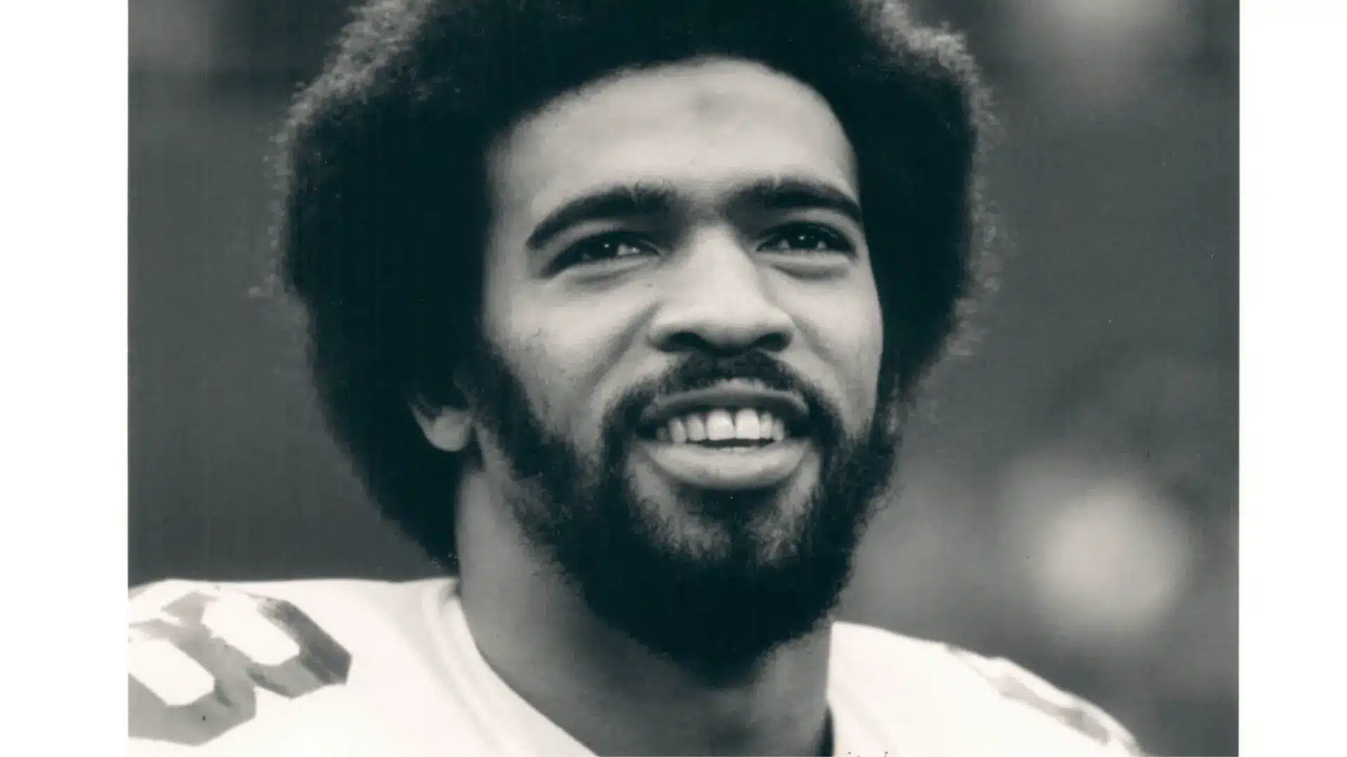 black and white close up portrait of a smiling football player wearing shoulder pads on field