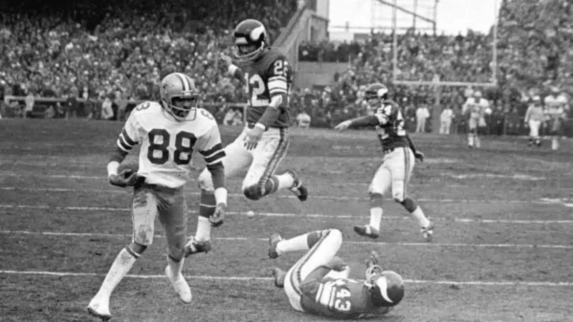 black and white game photo of a football player running past defenders after making a catch