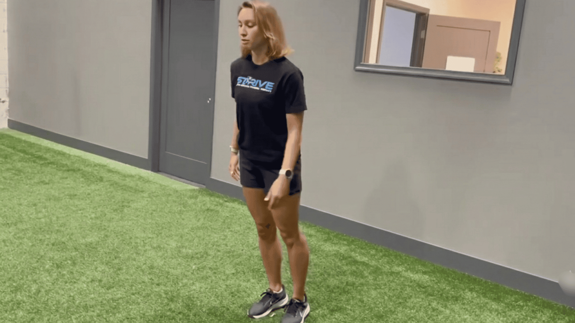 female athlete standing on indoor turf before a sprint drill in a sports training facility