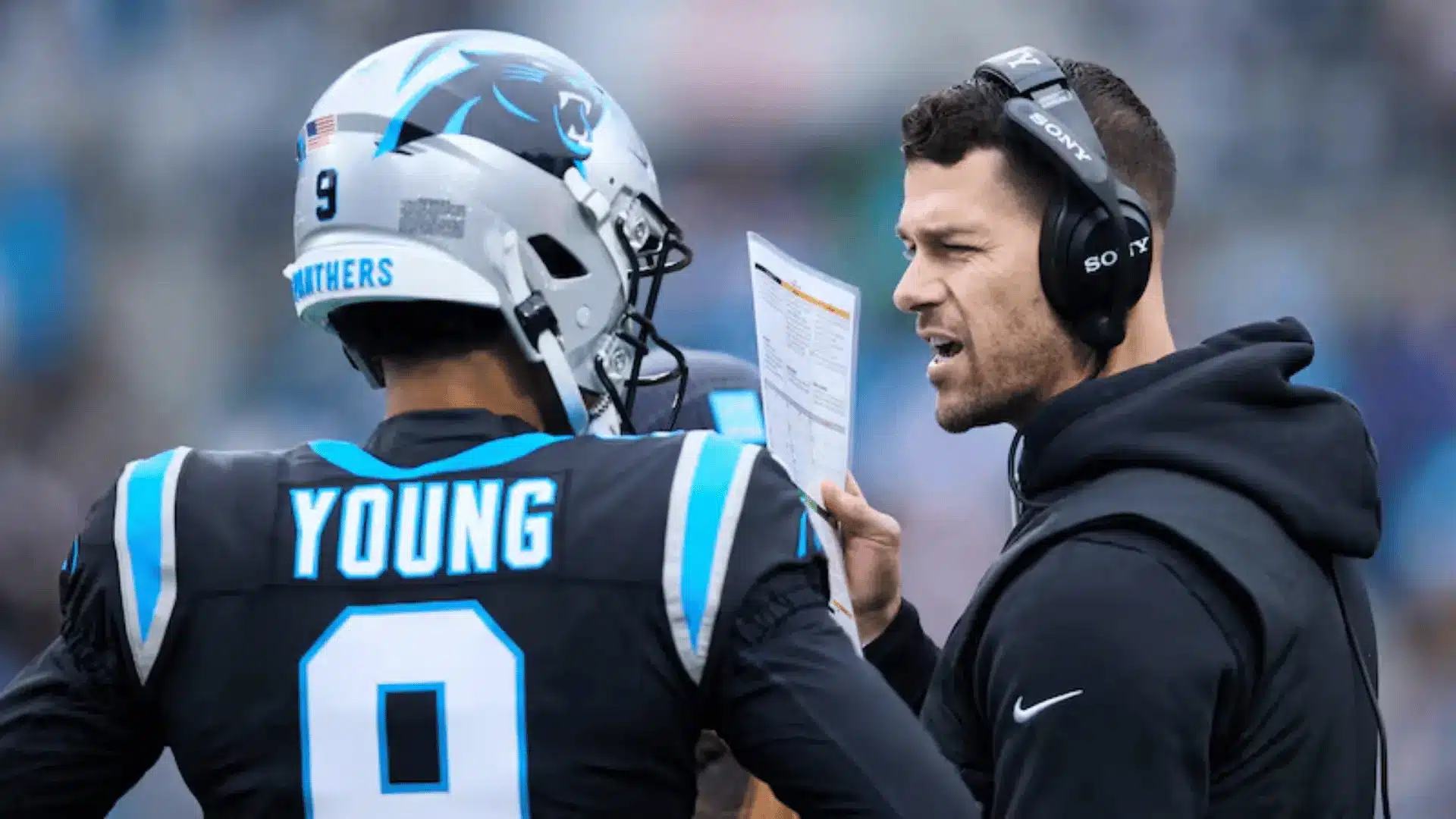 football coach speaking with quarterback on sideline while holding play sheet