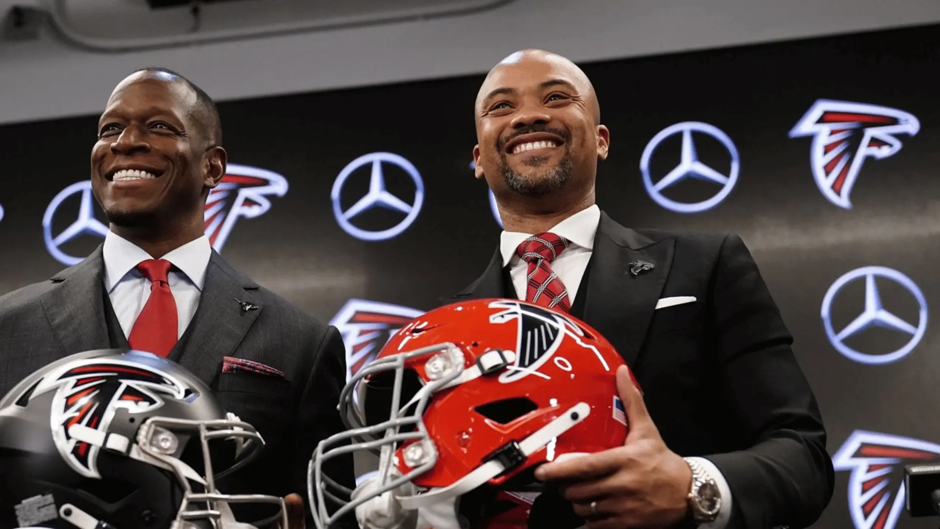 football executives holding team helmets during formal press event in front of sponsor wall