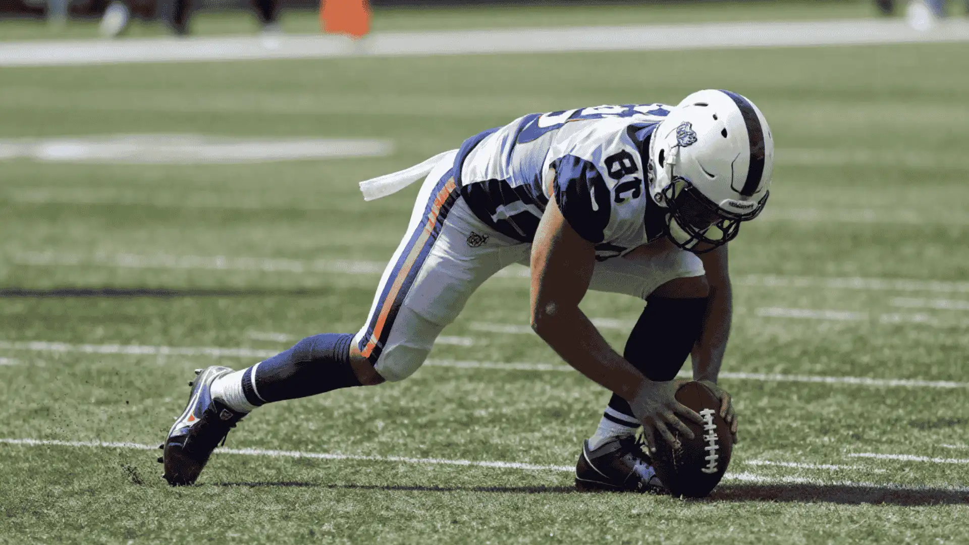 football player crouches low while placing both hands on the ball before a play on a sunny field
