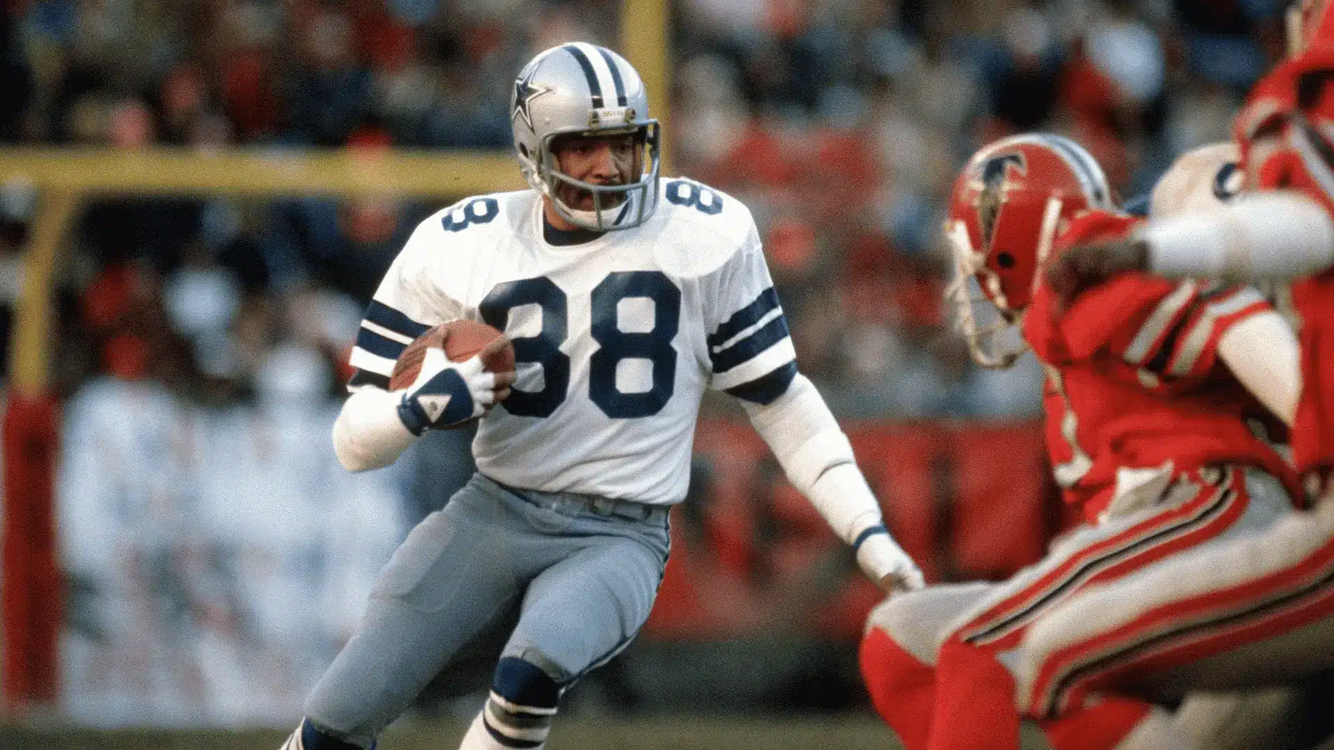 football player in white uniform runs with the ball toward defenders on a crowded stadium field