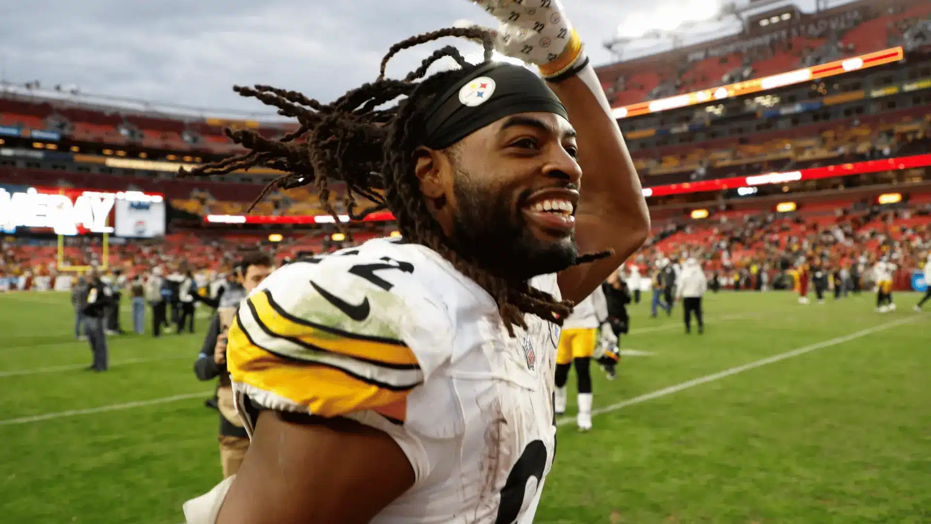 football player smiling and waving to fans after a game on a crowded stadium field