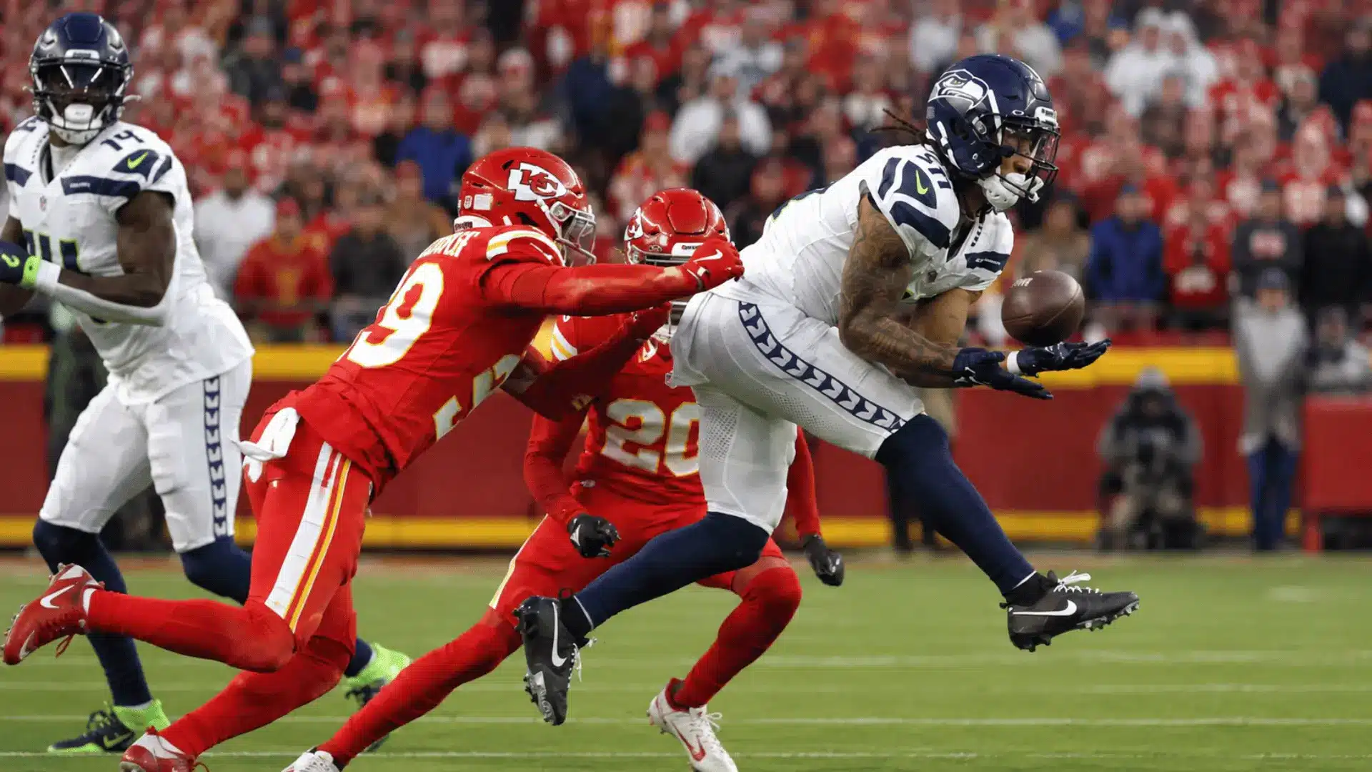football receiver in white uniform reaching for a pass while red defenders chase during a stadium game