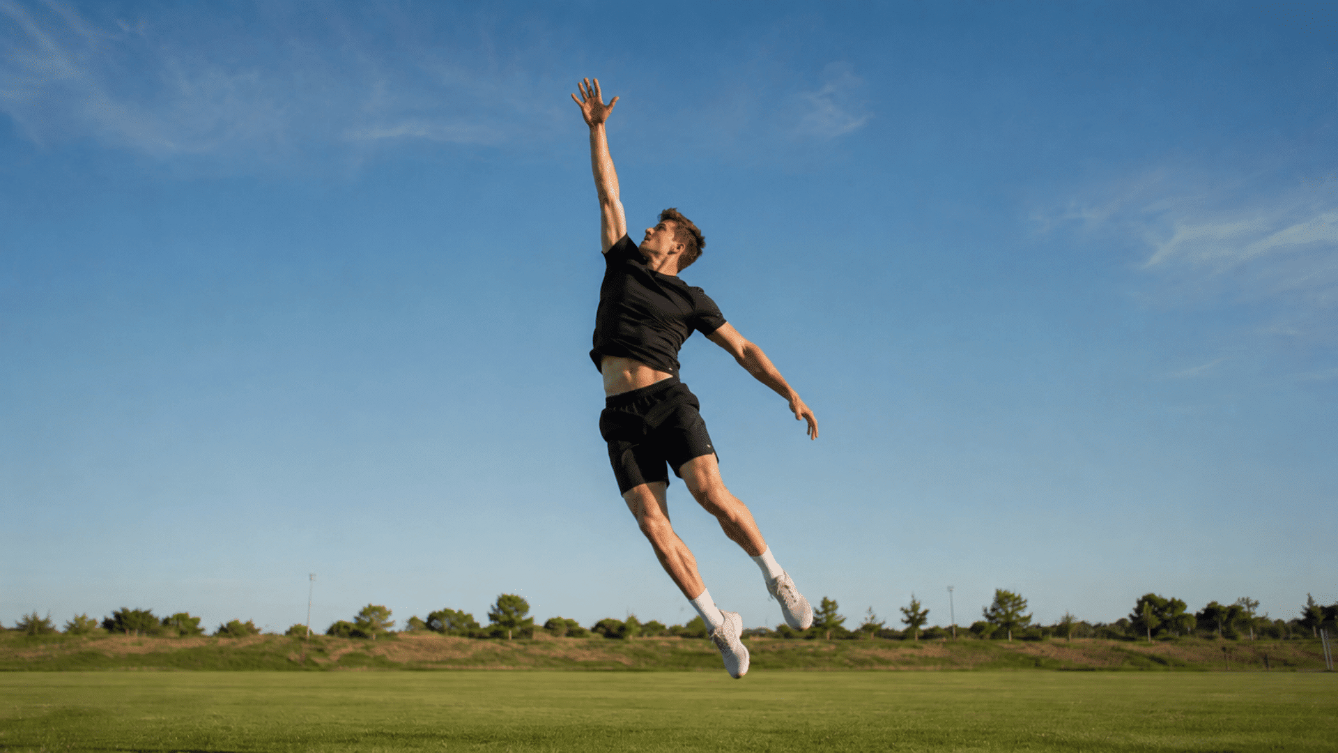 athlete performing a vertical jump on an open grassy field during bright natural sunlight