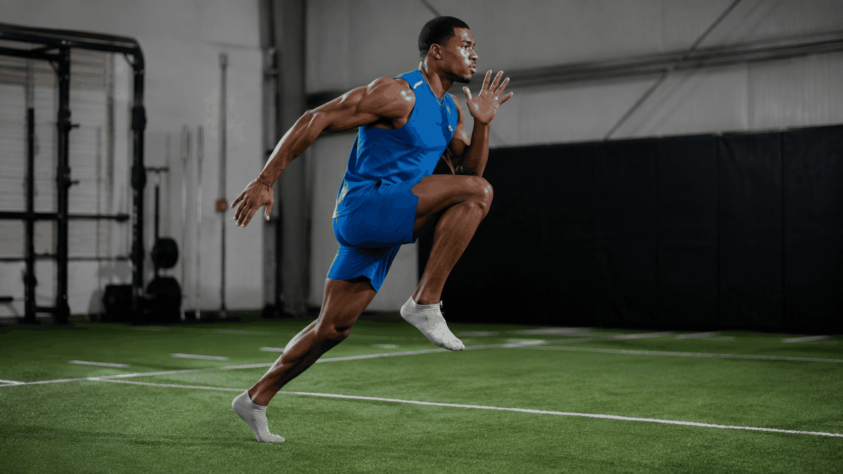 muscular man in blue athletic wear sprinting in socks on indoor green turf showing high knee drive