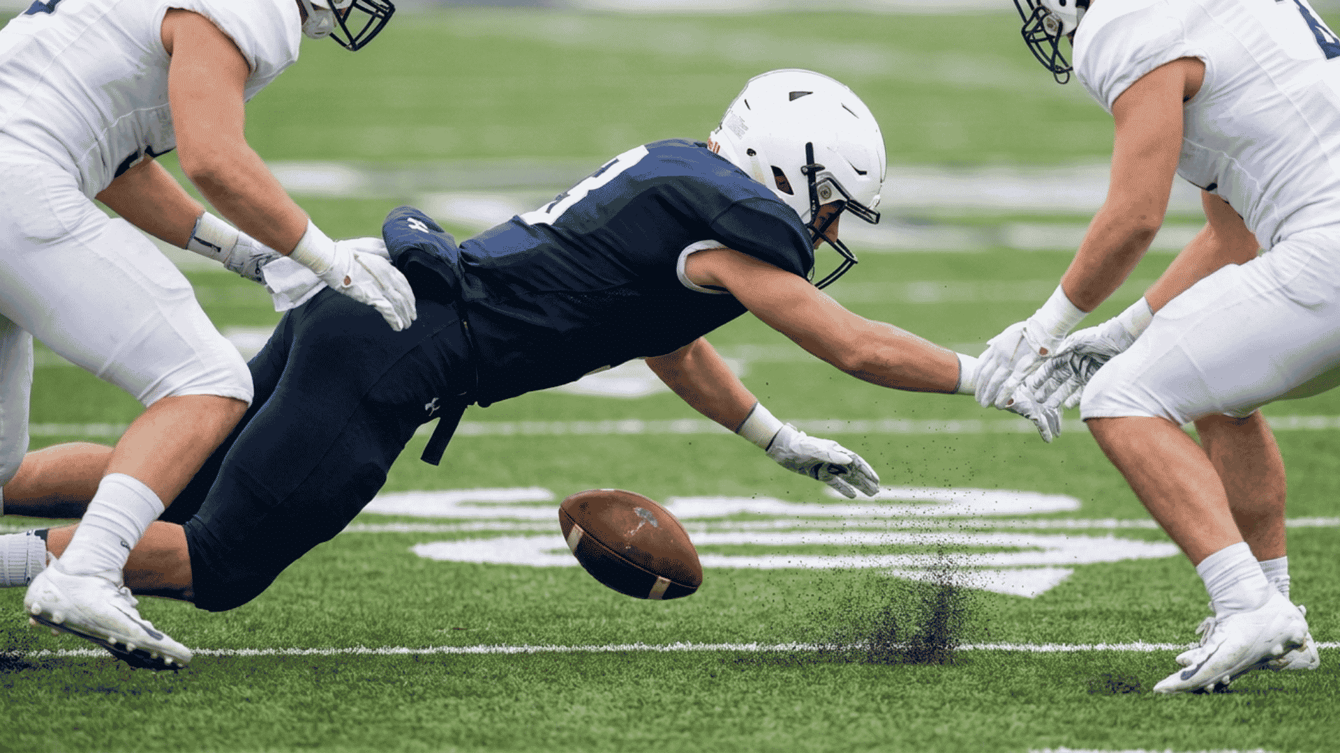 football player dives toward a bouncing onside kick while opponents close in