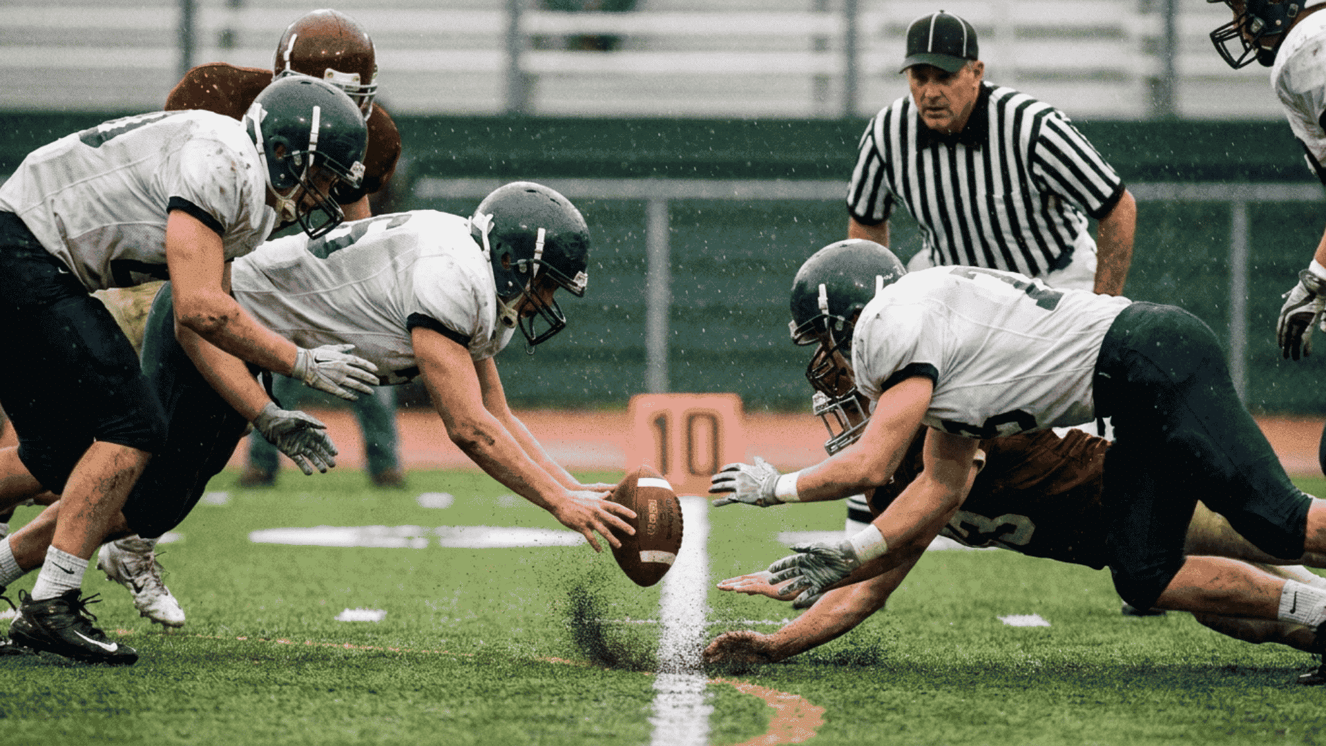 players dive toward a loose football as an official watches the recovery attempt