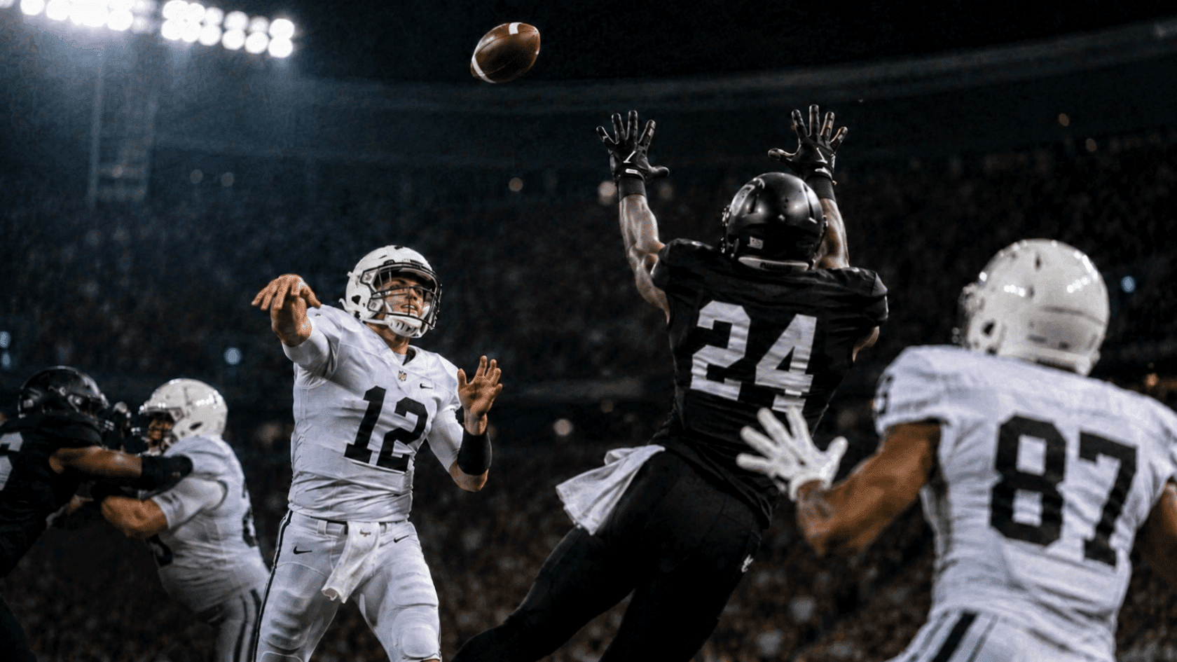quarterback throws as defender leaps to intercept the pass under bright stadium lights