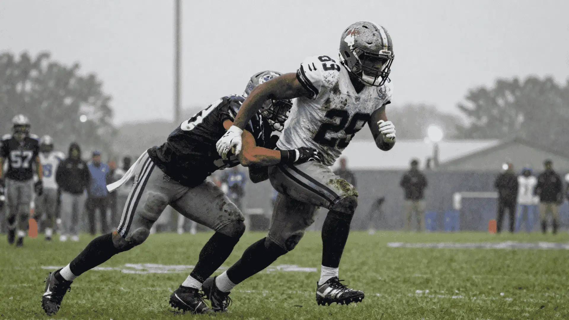 running back drives through contact while carrying the ball across a rain soaked football field