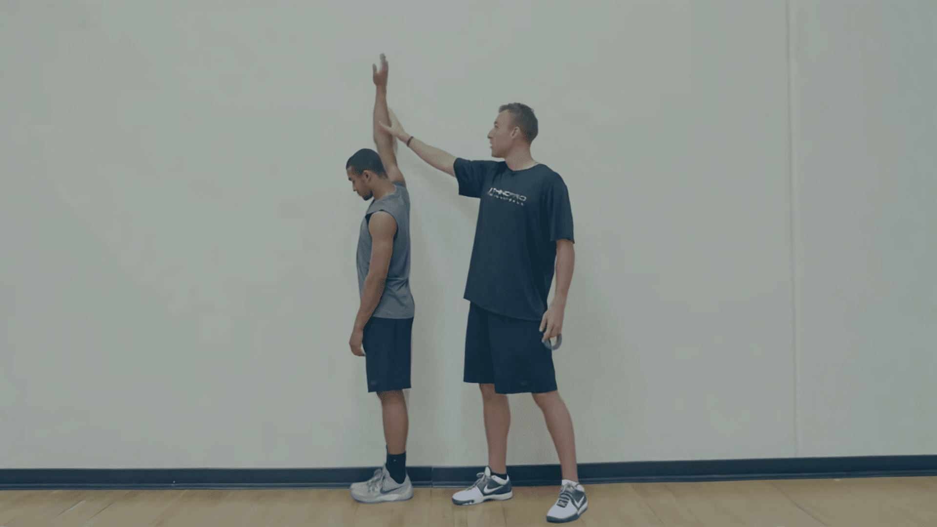 trainer measuring an athletes standing reach against a wall before testing vertical jump height
