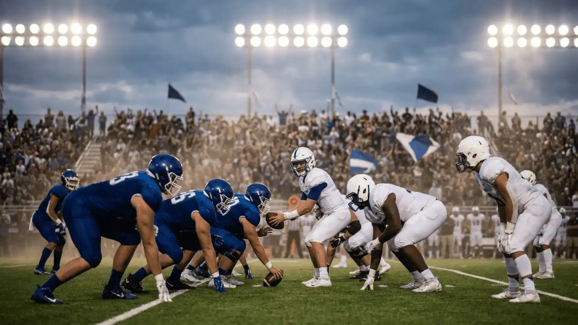 two football teams in blue and white uniforms line up before the snap under bright stadium lights