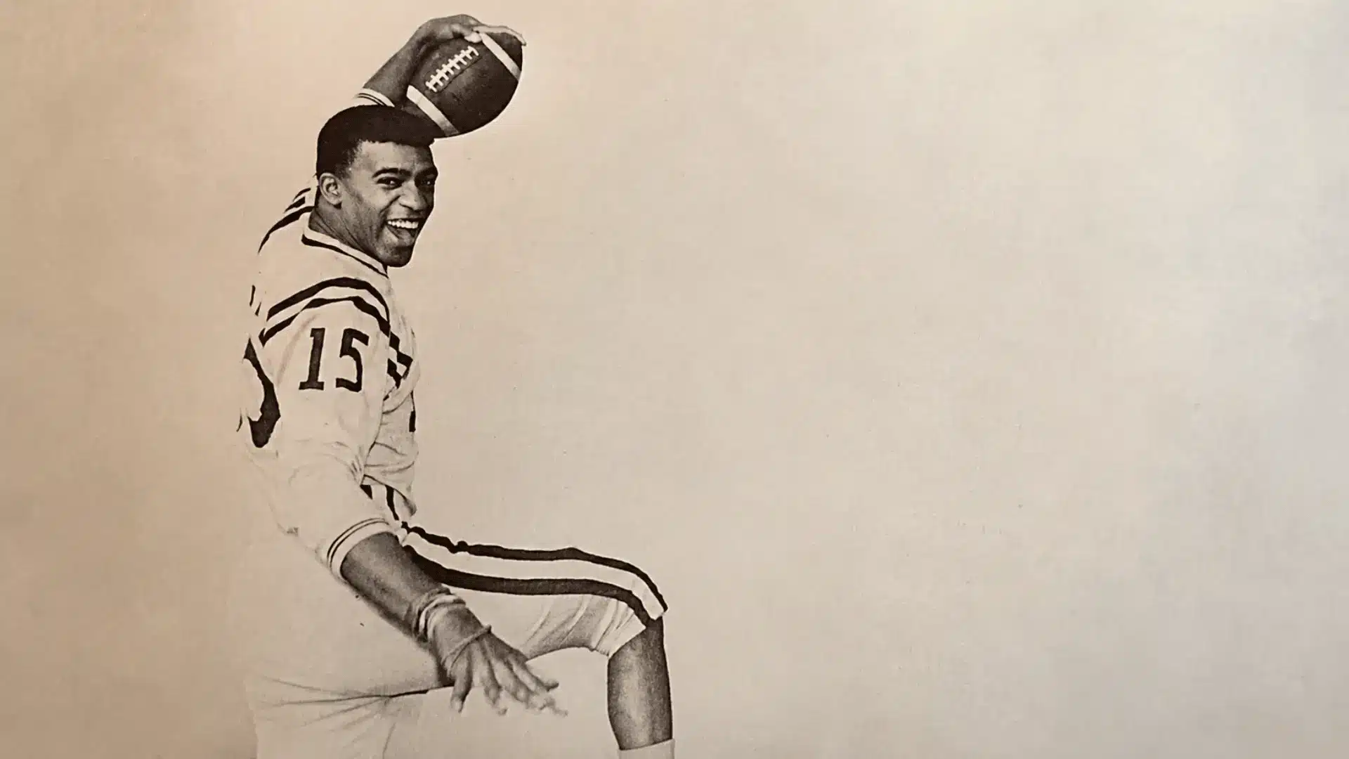 vintage football player smiles while balancing a football above his head in a playful pose