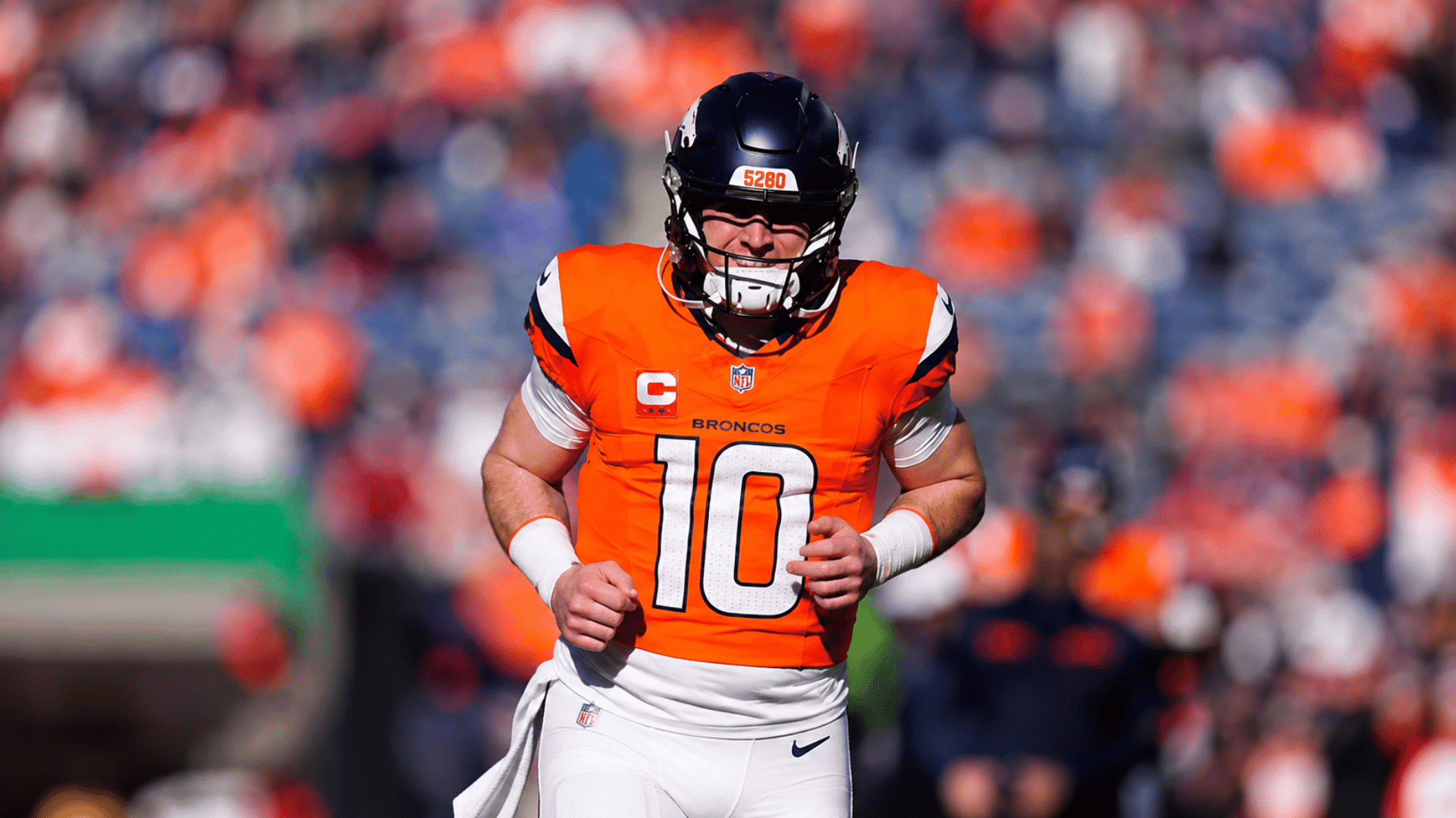 broncos quarterback in orange uniform runs forward with both hands positioned in front