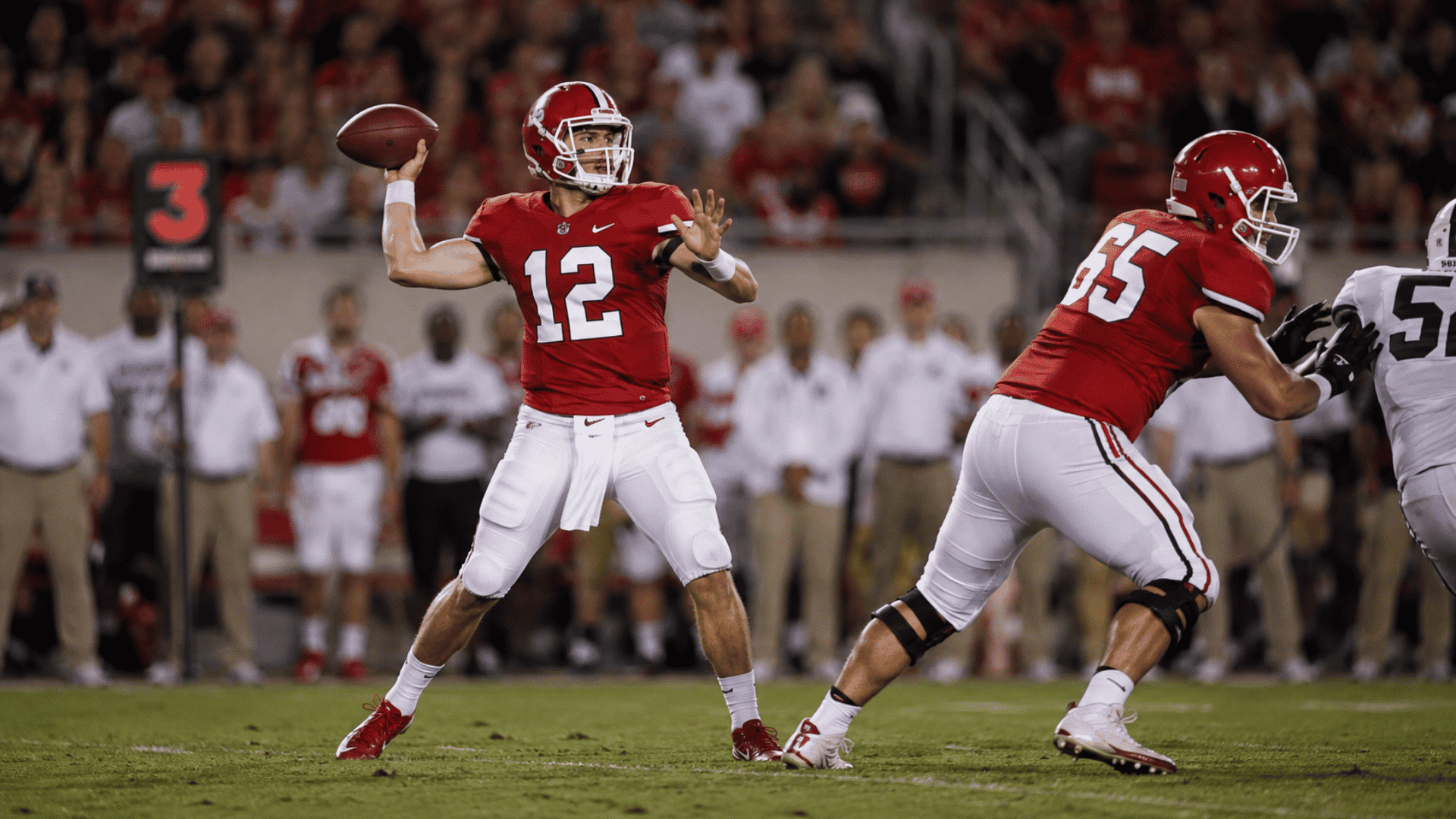 quarterback in red jersey prepares to throw as a lineman blocks during a football game at night