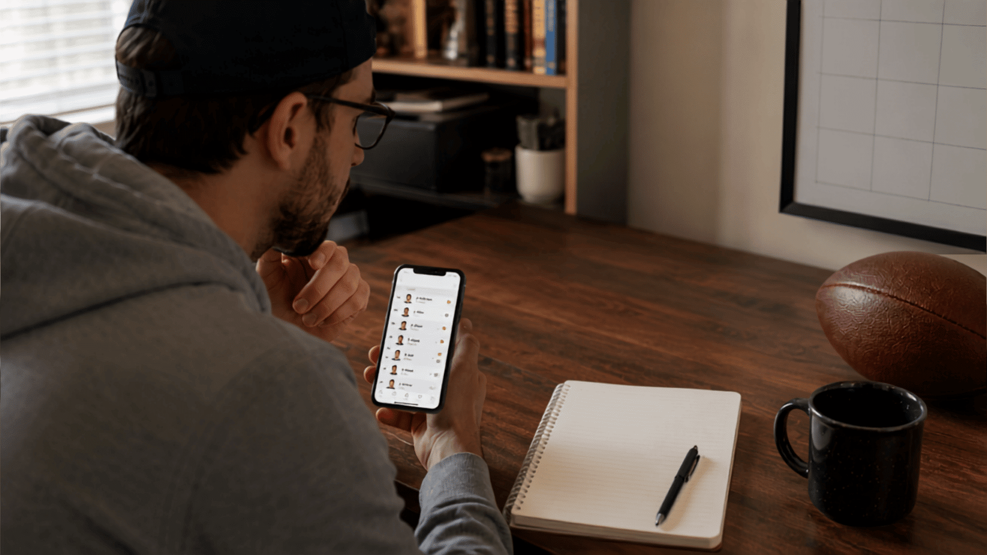 fantasy football manager checking lineup on phone beside notebook with trade notes and weekly schedule