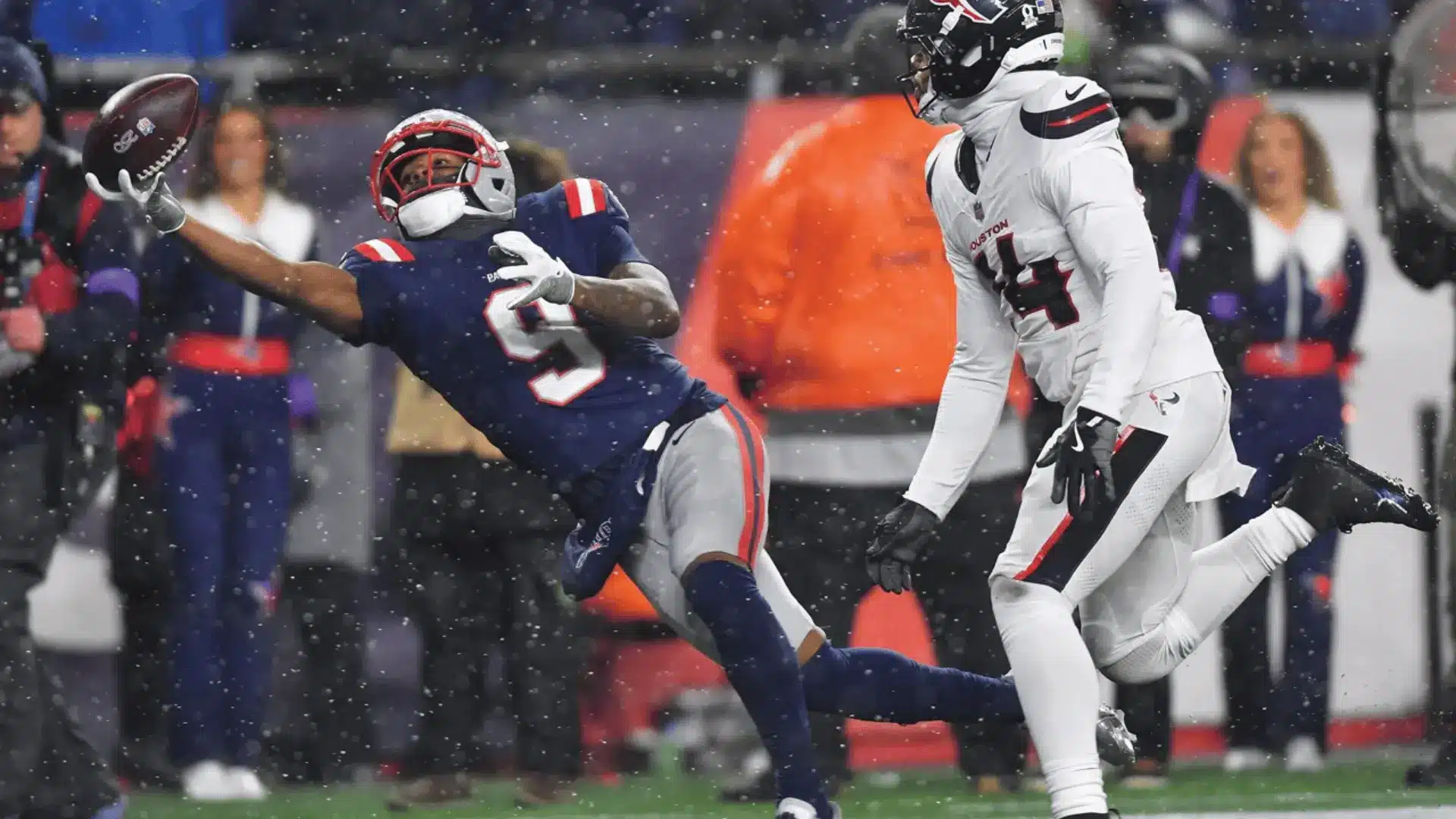 new england receiver reaching for a catch against an atlanta defender during a snowy game