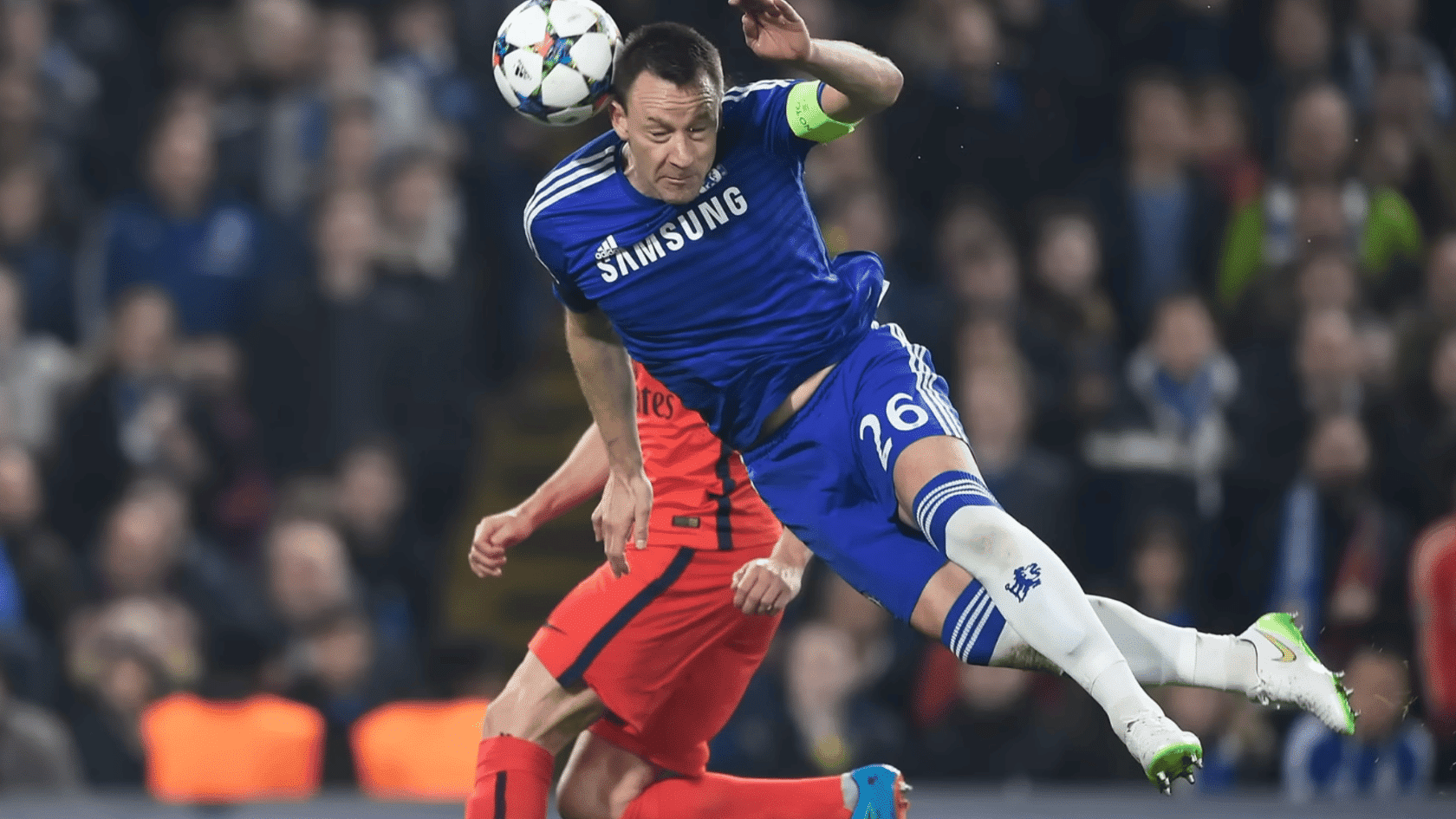 soccer player in blue kit heads the ball while colliding with an opponent in red during a match