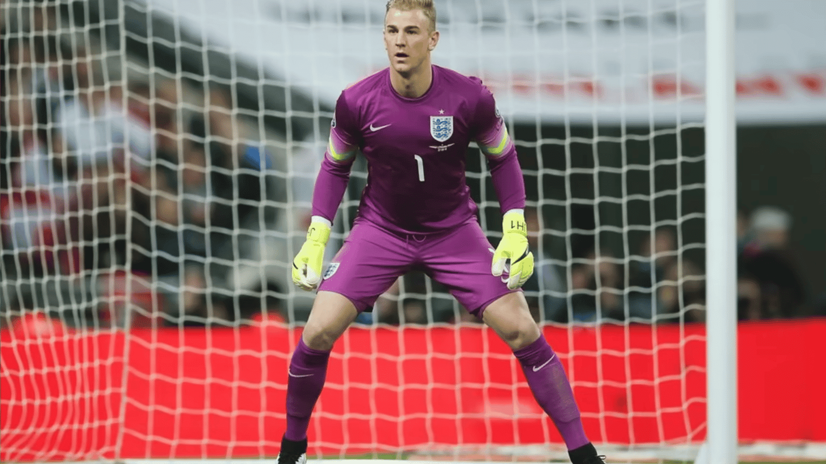 goalkeeper in purple uniform with yellow gloves standing alert in front of a soccer goal