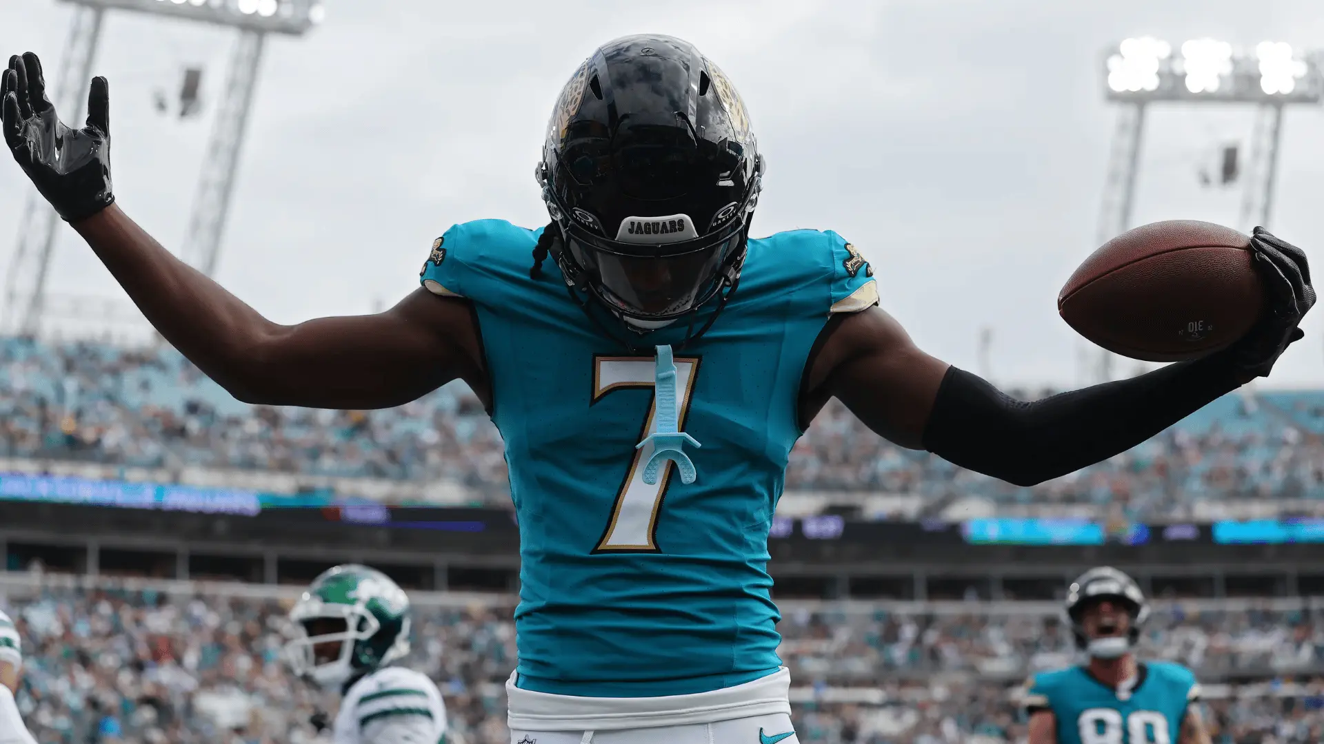 jacksonville football player in teal number seven uniform holding a ball with arms raised