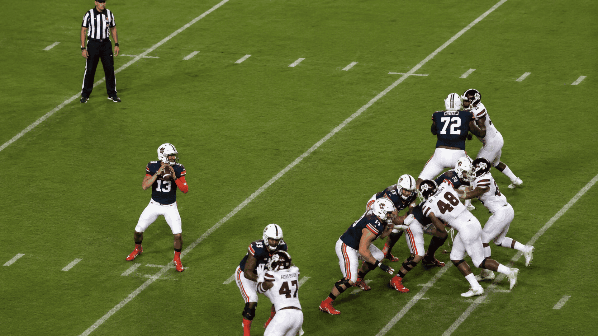 quarterback standing in the passing pocket as offensive linemen block rushing defenders on the field