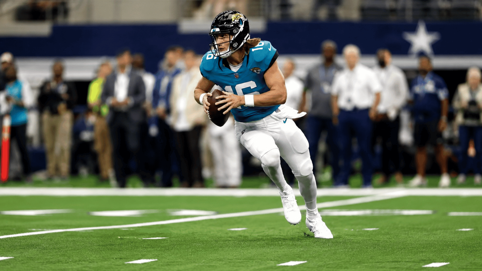 football quarterback in teal jersey runs with the ball across a bright indoor stadium turf