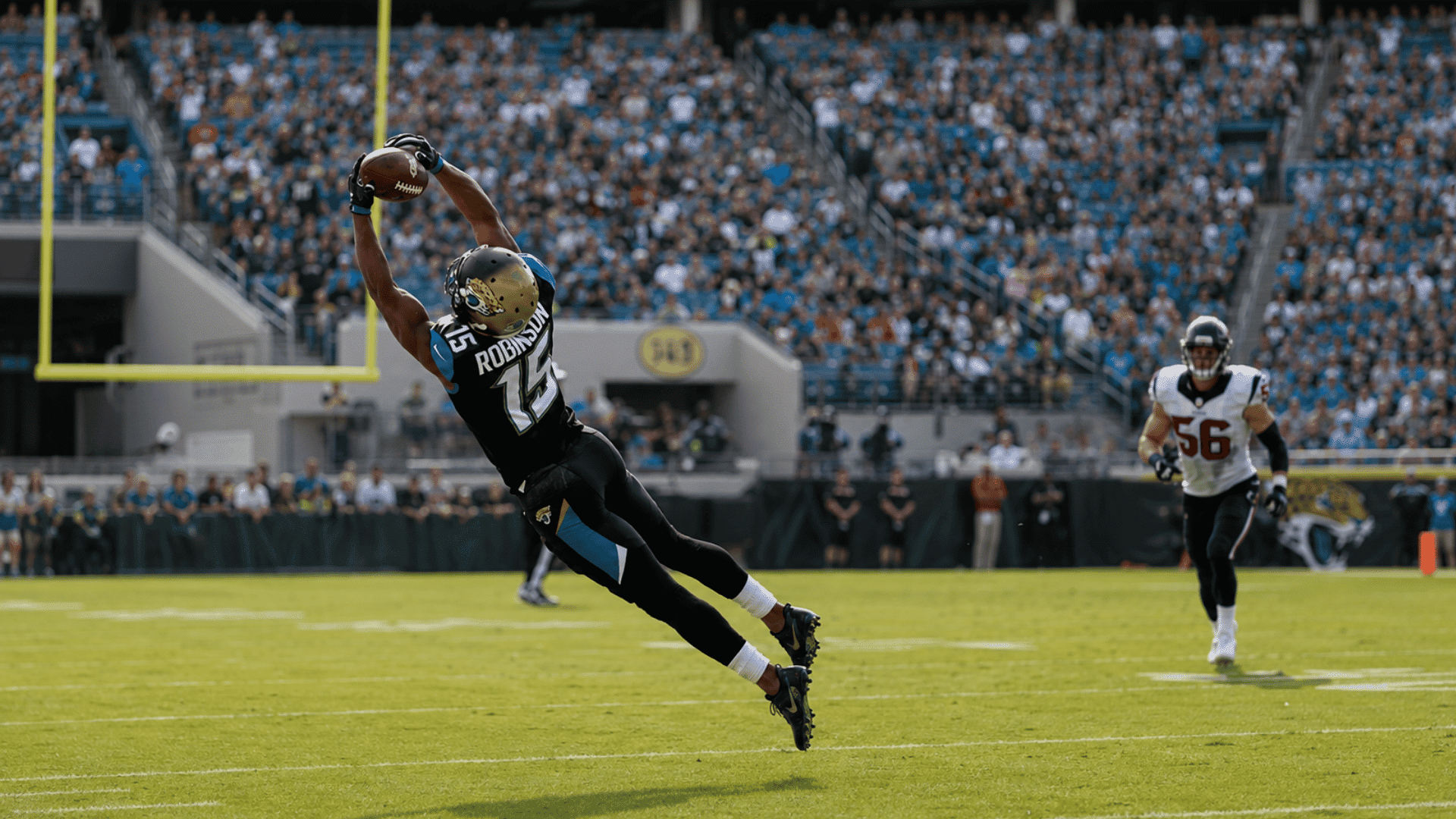 football receiver makes a diving catch while a defender trails behind in a packed stadium